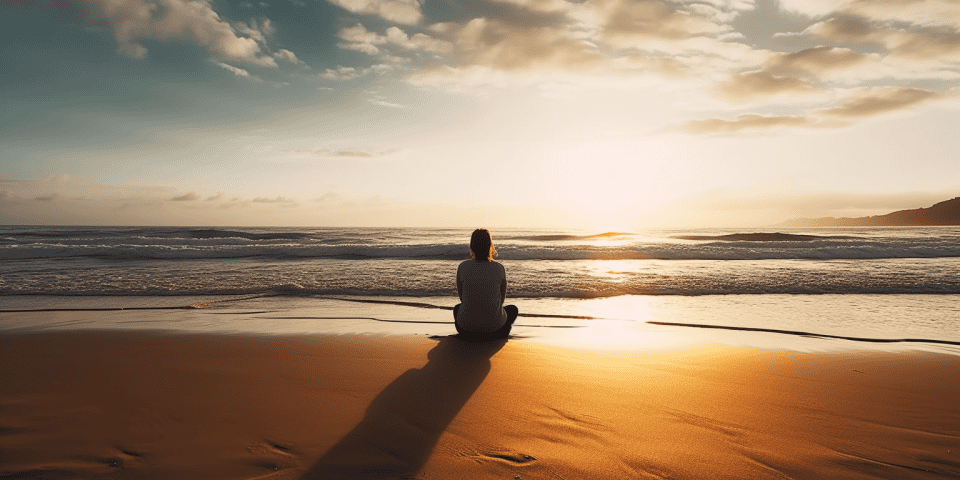A person sitting on a beach looking peacefully at the horizon