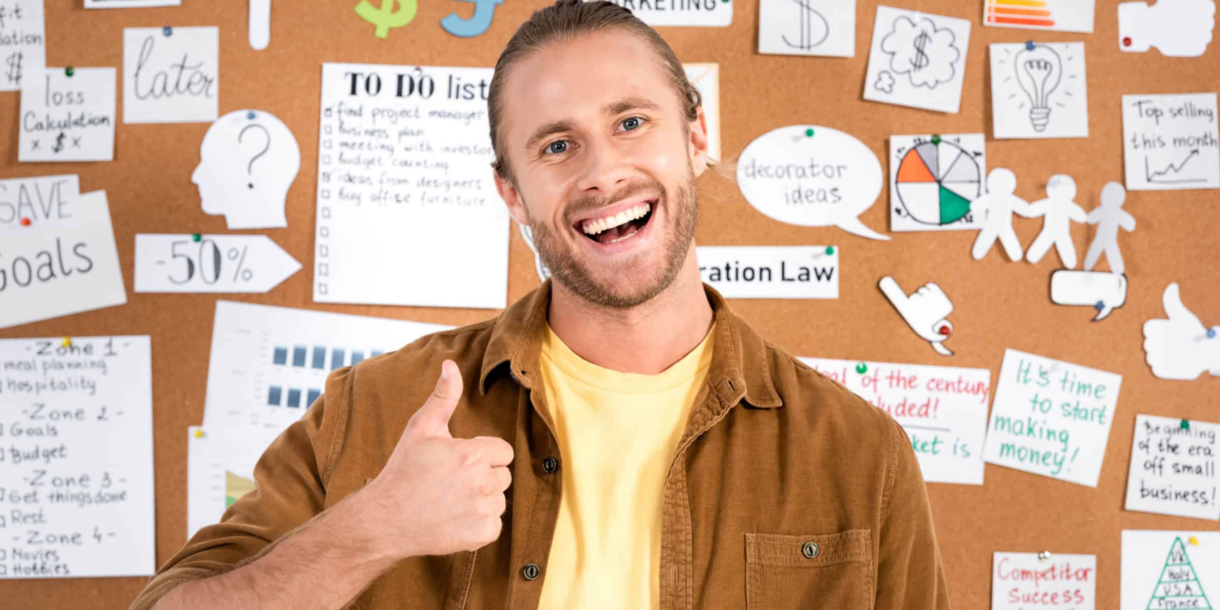 A man standing in front of a bulletin board with a thumbs up sign.