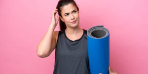 A young woman holding a yoga mat over pink background.