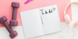A notebook with a to do list on it and a pair of pink dumbbells.
