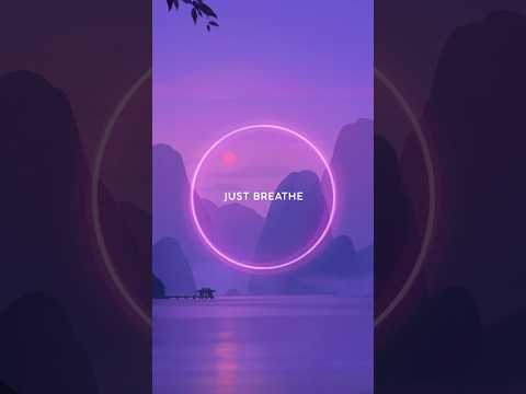 A glowing neon circle with the words “Just Breathe” overlays a serene purple landscape of mountains and water at sunset.