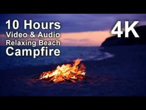 A campfire burns on a sandy beach at dusk with text overlay advertising a 10 hour 4K video and audio of a relaxing beach bonfire.